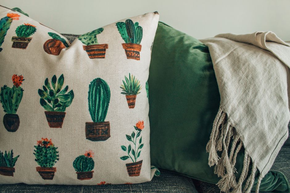 A cozy modern interior featuring cactus print throw pillows and a soft blanket on a sofa.